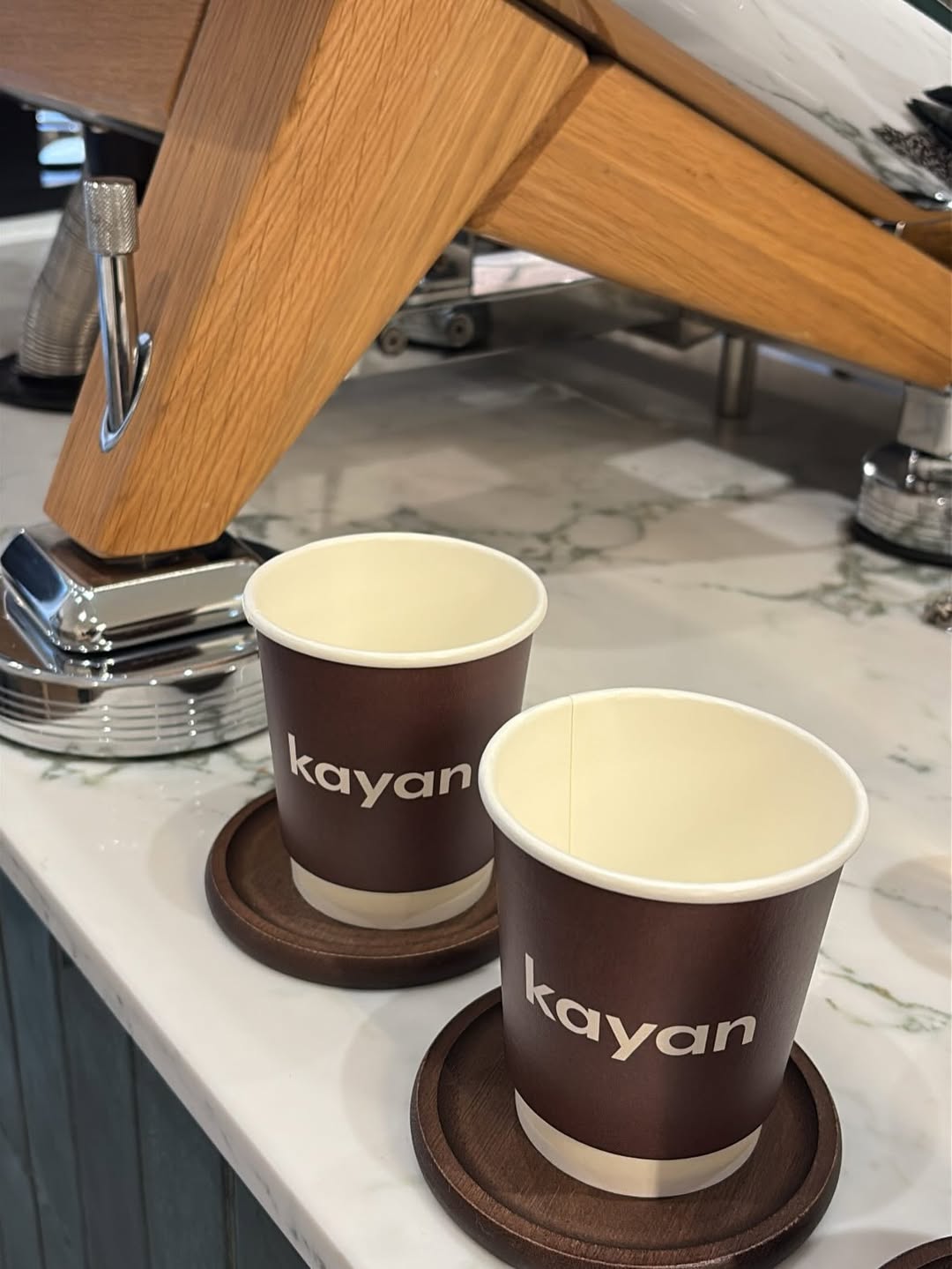Two Kayan Coffee cups on a marble counter beneath an espresso machine